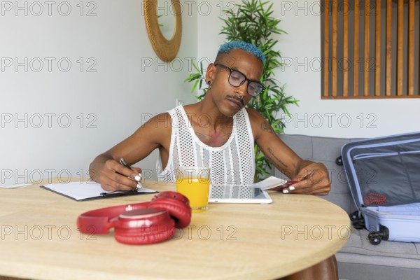 LGBTQIA+ person meticulously preparing for the holidays, planning with a notebook and tablet. A suitcase is ready, signifying excitement for upcoming travel
