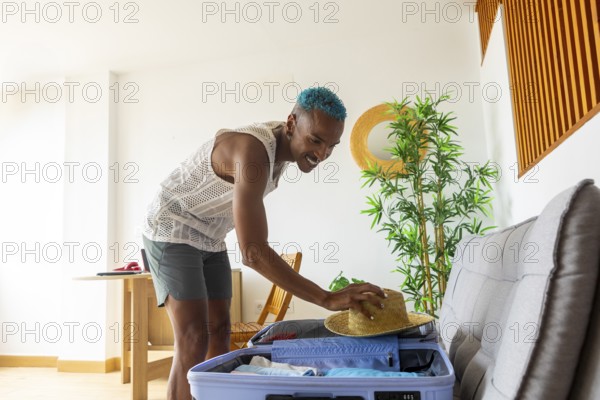 LGBTQIA+ man with teal hair packs a suitcase for a holiday, embodying joy and diversity. The bright room and casual summer attire convey excitement and freedom