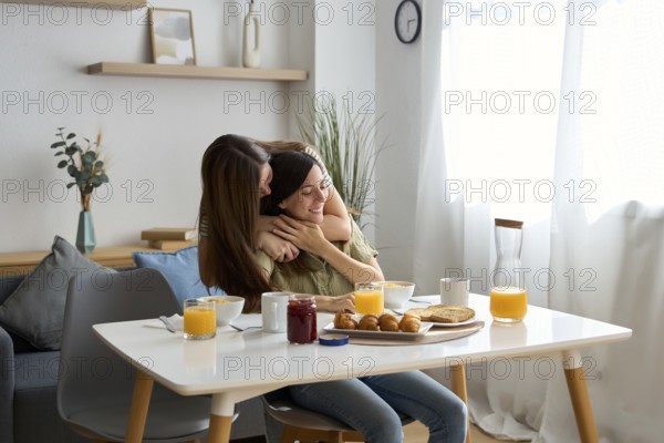 A loving lesbian couple shares a tender embrace while enjoying breakfast at a sunlit dining table The serene setting captures the warmth and intimacy of their relationship