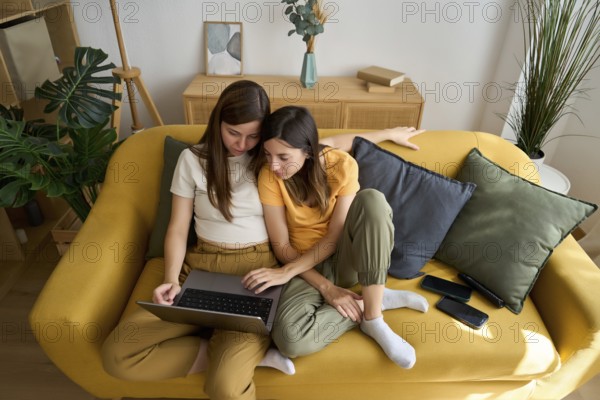 A warm scene captures a lesbian couple sharing a laptop on a cozy couch They seem comfortable and content, enjoying a quiet moment together in their stylish living room