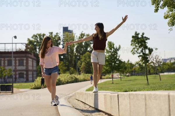 A joyful lesbian couple enjoys a sunny day, holding hands and balancing on a sidewalk in a park, embracing love and freedom Perfect representation of LGBTQIA+ pride