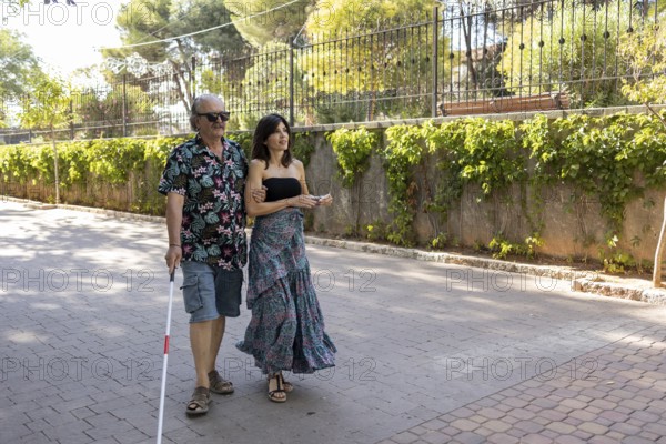 Photograph capturing a blind man using a white cane, being guided through town by his supportive daughter on a sunny day
