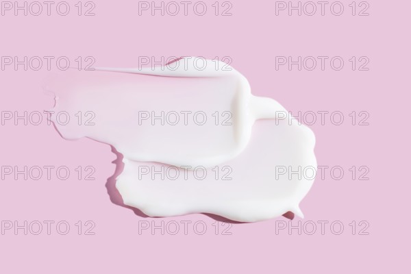 A delicate smear of creamy cosmetic product, displaying texture against a soothing pink background. Ideal for beauty and skincare themes