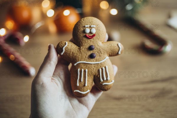 A hand holds a charming gingerbread man cookie decorated with icing Soft lighting and blurred holiday decor create a warm, festive ambiance Ideal for holiday themes