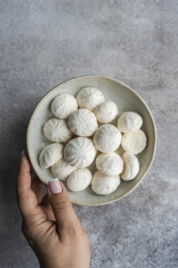 A hand holding a small ceramic bowl filled with handmade mini zephyr marshmallows, highlighting their delicate shape and soft texture in a cozy and minimalist setting