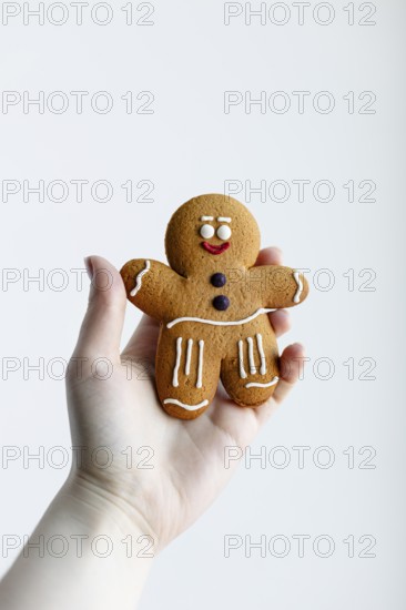 A hand holding a cheerful gingerbread man cookie, decorated with white and red icing, isolated against a clean white background Perfect for holiday or Christmas themes