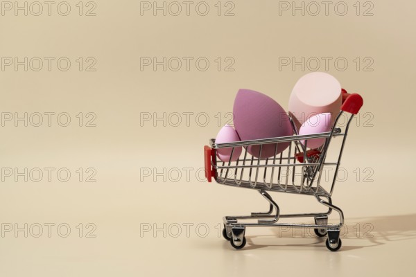 A collection of vibrant cosmetic sponges displayed in a miniature shopping cart against a soft pastel background Ideal for beauty, shopping, and skincare themes