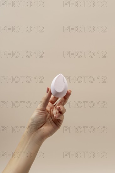 A hand gracefully holds a teardrop-shaped cosmetic sponge against a soft beige background, highlighting its smooth texture Ideal for beauty and makeup themes