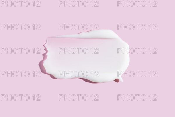 A dollop of white cream or gel cosmetic product smeared on a pastel pink background, depicting a rich and smooth texture