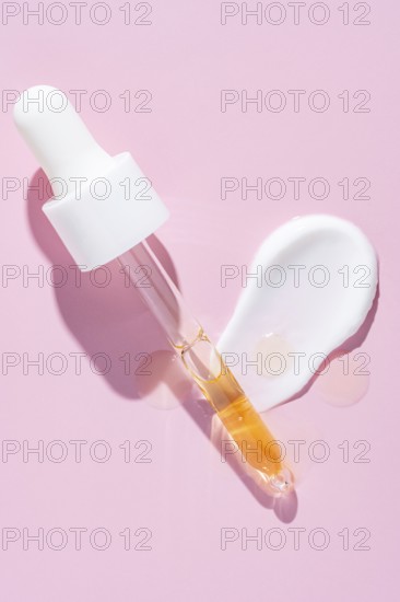 A dropper dispenses golden serum beside a white cream smear on a vibrant pink surface, representing skincare textures