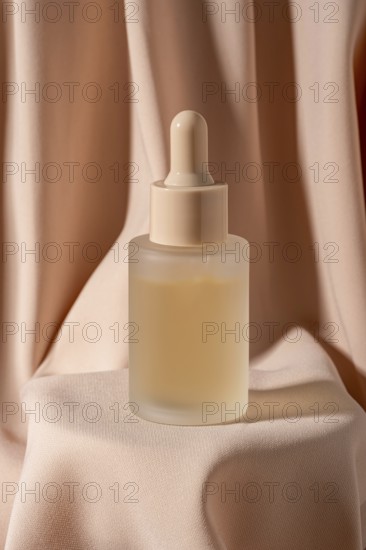 A minimalist frosted glass bottle with a dropper, containing skincare serum, is placed against luxurious soft fabric The warm beige tones create an elegant, calming ambiance