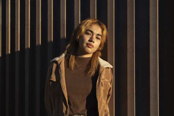 A Mixed-race woman leans against a textured wall, bathed in warm sunlight Her casual outfit and confident expression create a harmonious and modern visual contrast