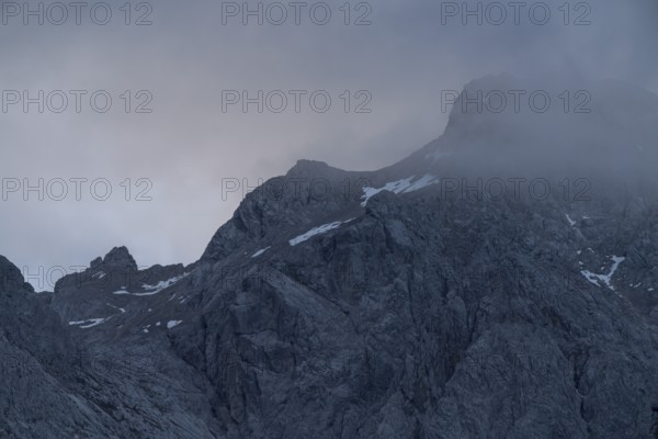 A dramatic view of towering peaks in the Bavarian Alps, partially covered by swirling mist The rugged landscape exudes a sense of mystery and grandeur, perfect for nature and adventure themes