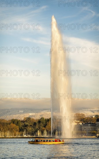 The iconic Jet d'Eau fountain in Geneva, Switzerland, captured during autumn with golden light, a scenic lake view, and a boat in the foreground adding a serene touch