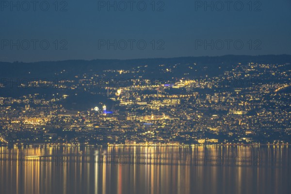 A captivating nighttime view of Lausanne, Switzerland, with the city lights reflecting on the calm waters of Lake Geneva The scene highlights the vibrant urban skyline under a clear night sky