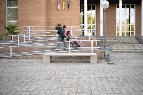 A college couple navigates a ramp on campus, highlighting accessibility The woman, in a wheelchair due to spina bifida, shows resilience and support from her partner