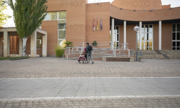 A couple traverses a college campus, highlighting accessibility and inclusion The woman, coping with spina bifida, uses a wheelchair as they move by modern buildings