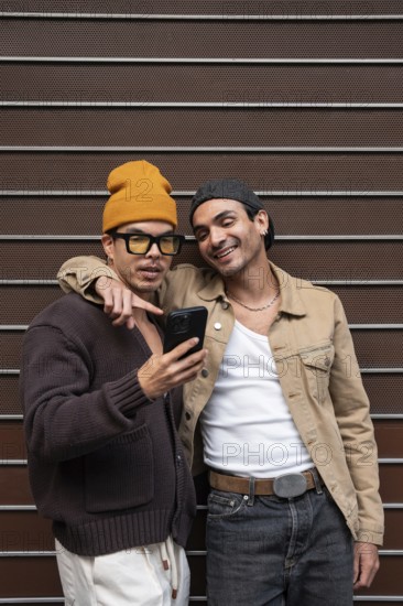 A joyful couple stands close together, sharing a moment and viewing something exciting on a smartphone. Their casual attire and warm smiles exude happiness and connection