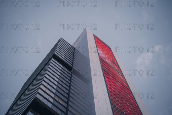 Low-angle view of a modern skyscraper with a striking red facade against a clear sky. The sleek architecture embodies urban sophistication and city life