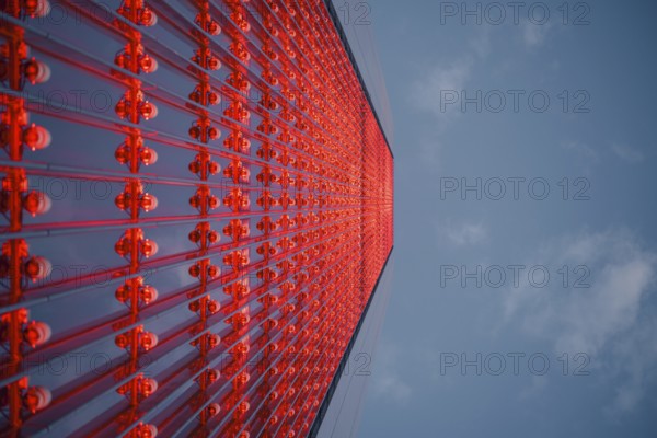 Dramatic upward view of a skyscraper with a red glass facade against a blue sky. The modern architectural design and vibrant colors create a stunning urban scene