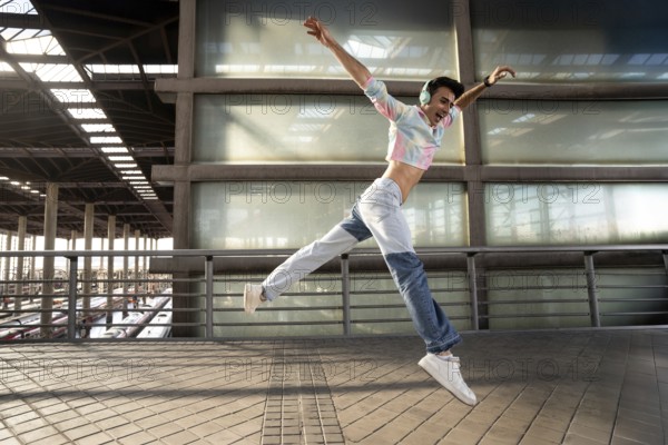 A young person in vibrant attire and headphones joyfully jumps in mid-air on an urban walkway, with a modern glass and concrete backdrop, capturing movement and freedom