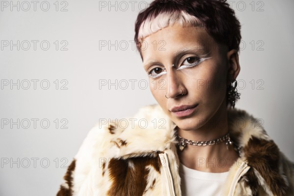 A portrait featuring a woman looking at camera with bold white eye makeup and piercings, wearing a stylish fur coat and jewelry, against a neutral background conveying confidence and individuality