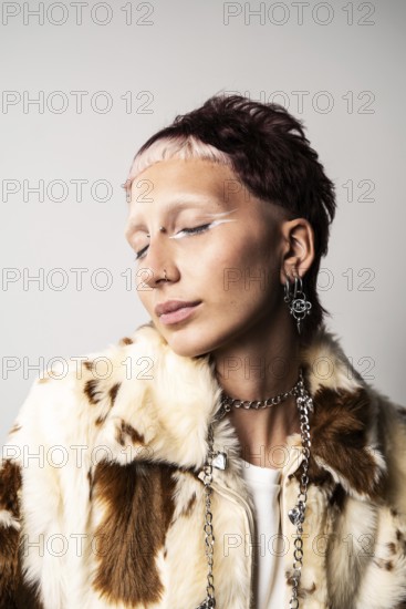 Close-up of a woman with a bold hairstyle, glamorous nose and ear piercings, striking white eyeliner, and a faux fur jacket and closed eyes creating a modern fashion statement