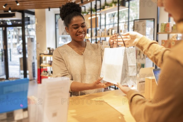 A customer service assistant in a bright cosmetics store smiles while handing a shopping bag to a patron. The store features well-lit shelves with beauty products