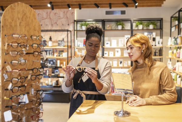 A retail employee helps a customer choose eyeglasses in a stylish boutique. The modern store is stocked with beauty products, and a display of eyewear is arranged neatly on the counter