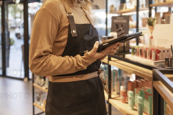 A worker in a cozy cosmetics store checks inventory using a tablet. The store is warmly lit, with neatly arranged products on shelves, creating an inviting atmosphere