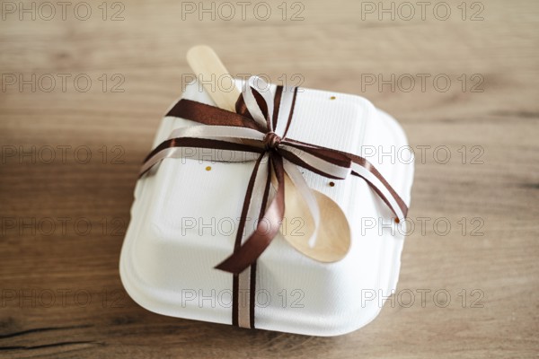 Elegantly packaged bento birthday cake in a white takeout box adorned with a chocolate-brown ribbon and wooden spoon, ideal for gifting