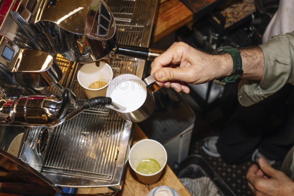 A skilled barista pours steamed milk from a metal pitcher into a cup of freshly brewed espresso, showcasing the art of specialty coffee preparation in a cozy coffee shop setting