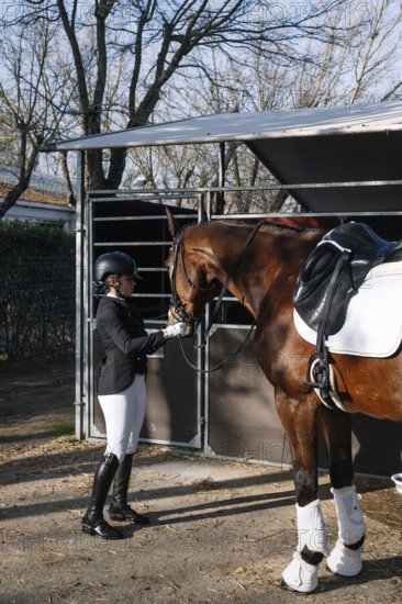 A rider in traditional attire prepares a horse in a stable for a classical dressage performance, highlighting the elegance and discipline of this equestrian sport