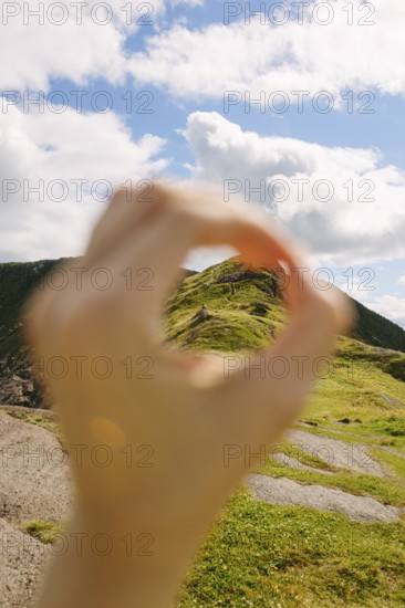 A creative shot capturing a distant hiker through an O-shaped hand frame against the lush, green landscape of Middle Cove, Newfoundland. The focus on natural beauty and perspective invokes a sense of exploration and appreciation of the outdoors