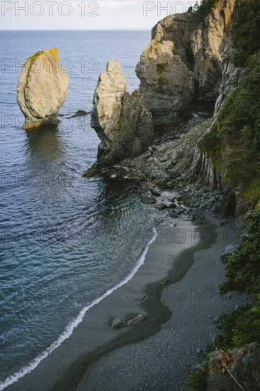 A breathtaking coastal view of Sherwink, Trinity, Newfoundland capturing the waves gently lapping against a secluded pebble beach surrounded by towering rugged cliffs and distinctive sea stacks
