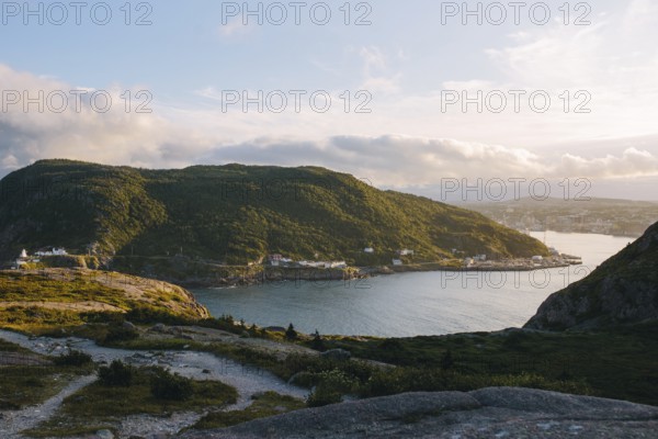 A serene view of Signal Hill, St. John's showcasing a sweeping coastline with a sunlit harbor nestled between lush, green hills during the golden hour in Newfoundland & Labrador, Canada