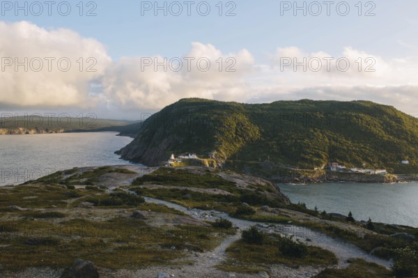 A serene sunset casts warm light over the rugged landscape of Signal Hill, St. John's, showcasing a panoramic view of steep cliffs and a peaceful bay. This picturesque scene captures the untouched natural beauty of Newfoundland & Labrador, Canada