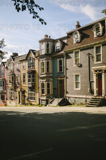 Historic row houses lining a peaceful street in St. John's, Newfoundland and Labrador, Canada, showcasing a variety of vibrant facades and architectural details under a clear blue sky