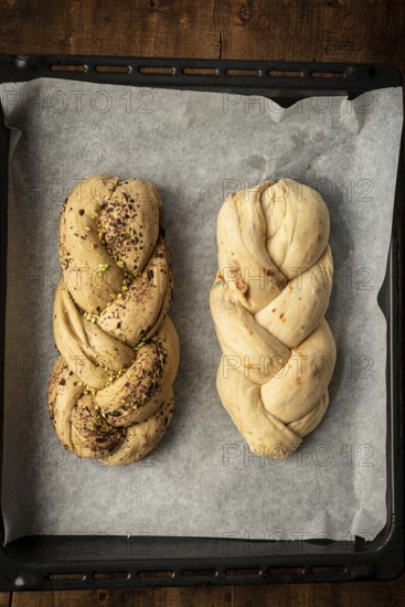 Top view of freshly baked Bakbah breads on parchment paper, featuring one loaf topped with pistachios and spices, and the other subtly infused with chocolate