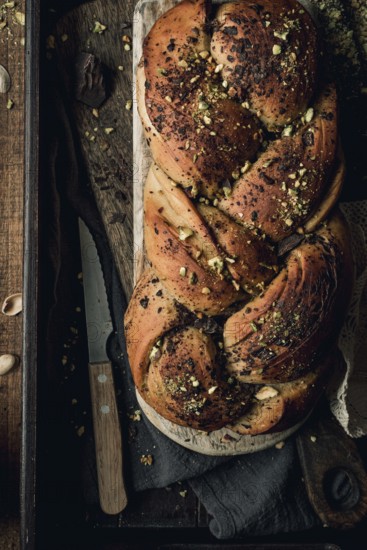 Top view of an artisanal chocolate and pistachio bakbah bread, beautifully presented on a dark wooden board with a knife beside it, enhanced by a sprinkle of pistachio chunks