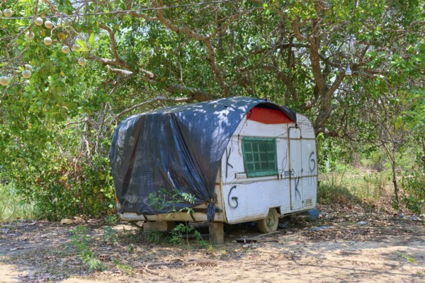An old caravan with black cover stands in a rustic landscape under trees, Pantanal, Mato Grosso, Brazil