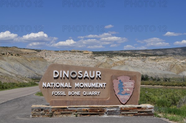 Dinosaur National Monument entrance sign with stone landscape in background under blue sky, Dinosaur National Monument, Utah, USA