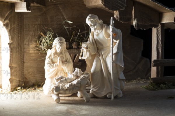 The Holy Family at the crib, wooden crib figurines represent the birth of Jesus Christ Child lying in a crib in a stable as a little Christ Child, Christmas