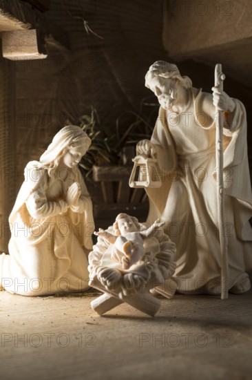 The Holy Family at the crib, wooden crib figurines represent the birth of Jesus Christ Child lying in a crib in a stable as a little Christ Child, Christmas