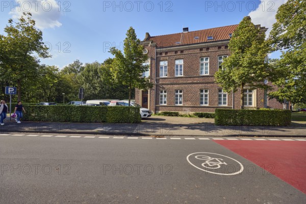 Bicycle road, brick houses, commercial buildings, job center, registry office, parking lot with cars, trees, hedge, blue sky, cumulus clouds, street Steverstraße, Lüdinghausen, Münsterland, Coesfeld district, North Rhine-Westphalia, Germany