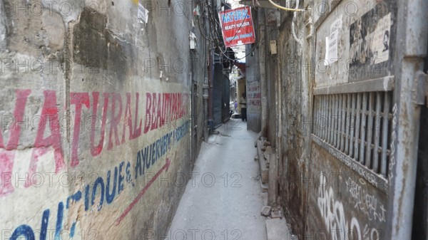Narrow urban alley with colorful advertising banners and graffiti on the walls, Delhi, India