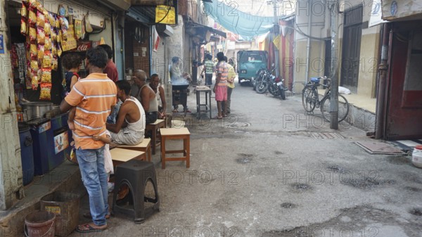 People look at a small kiosk on a road bike, busy street scene with people and shops, in an urban environment with moped and bicycle, Delhi, India