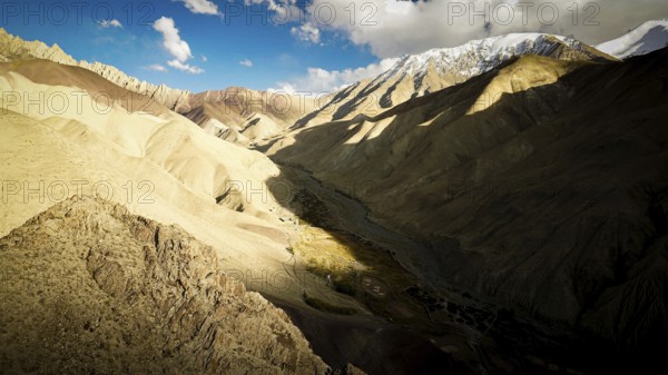 Dramatic mountain landscape with strong light and shadow in the valley, snow-capped mountains in the background, trekking in Ladakh, Stok la, Himalayas, India