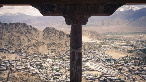 View from a window of the Leh Palace over Leh in a valley with surrounding snow-capped mountains and cloudy sky, trekking in Ladakh, Himalayas, India