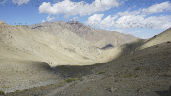 Wide mountain valley under a partly cloudy sky with a small path, trekking in Ladakh, Stok la, Himalayas, India